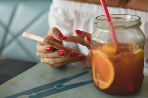 Woman checking her phone next to an iced tea